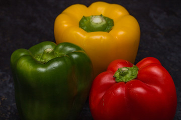 Close up of green pepper, red pepper and yellow pepper on a wooden chopping board
