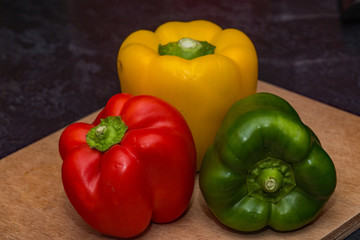 Red pepper green pepper and yellow pepper on a wooden chopping board