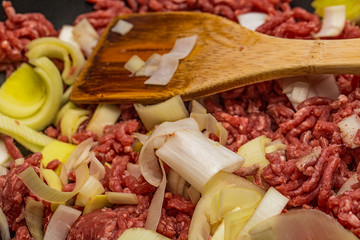 Close up of minced beef steak and leeks in a frying pan with a wooden spoon