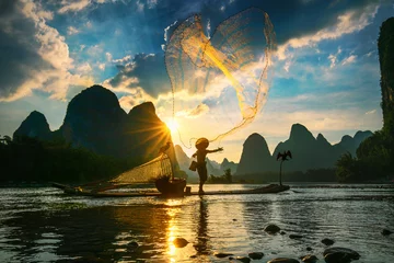 Crédence de cuisine en verre imprimé Guilin Silhouette de pêcheur de cormoran utilisant le filet sur le bateau en bambou antique