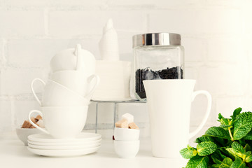 Tea drink concept. Piece of cafe, restaurant interior with teapot, tea cups, sugar cubes, tea leaves, paper napkins, saucers on white board against white brick wall.