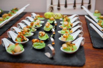 Seafood appetizers in porcelain spoons on black stone platter