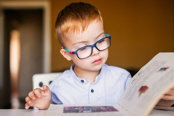 Cute toddler boy with down syndrome with big glasses reading intesting book