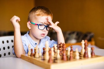 Ginger boy with down syndrome with big glasses playing chess at home