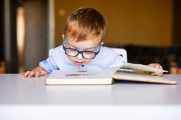 Cute toddler boy with down syndrome with big glasses reading intesting book