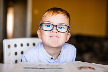 Cute toddler boy with down syndrome with big glasses reading intesting book