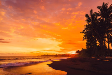 Bright sunset or sunrise with ocean waves and coconut palms in Bali, Keramas