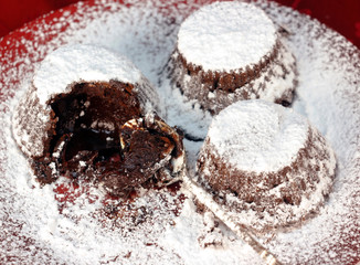 three dessert cakes fondants on a plate sprinkled with powdered sugar
