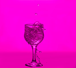Splashes of water. Glass on a pink background. Minimal night party life concept