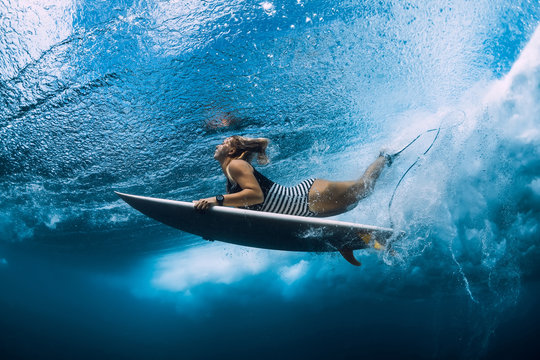 Surfgirl with surfboard dive underwater with under ocean wave.