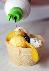 Pouring chocolate syrup on ice cream in waffle bowl
