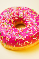 Bright donut in a pink glaze with a multi-colored rainbow sprinkle on a yellow background. 
