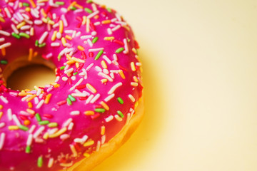 Bright donut in a pink glaze with a multi-colored rainbow sprinkle on a yellow background. 