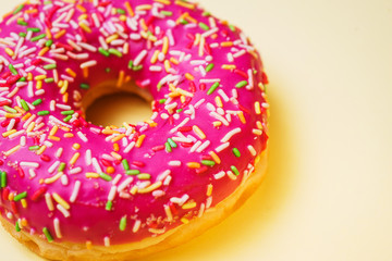Bright donut in a pink glaze with a multi-colored rainbow sprinkle on a yellow background. 