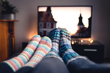 Couple with socks and woolen stockings watching movies or series on tv in winter. Woman and man sitting or lying together on sofa couch in home living room using online streaming service in television