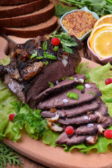 Baked ham of elk meat cut into slices topped with greenery and cranberries on the salad leaves