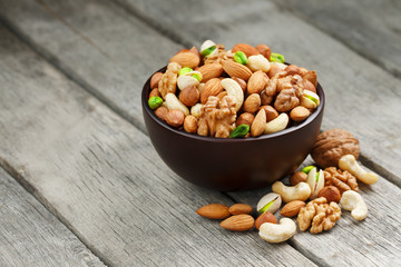 Wooden bowl with mixed nuts on a wooden gray background. Walnut, pistachios, almonds, hazelnuts and cashews, walnut.