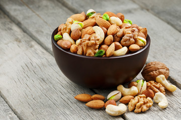 Wooden bowl with mixed nuts on a wooden gray background. Walnut, pistachios, almonds, hazelnuts and cashews, walnut.
