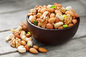 Wooden bowl with mixed nuts on a wooden gray background. Walnut, pistachios, almonds, hazelnuts and cashews, walnut.