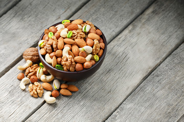 Wooden bowl with mixed nuts on a wooden gray background. Walnut, pistachios, almonds, hazelnuts and cashews, walnut.