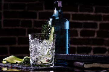 Gin-tonic alcoholic cocktail. Cucumber, rosemary, ice. On a black wooden background.