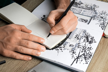selective focus of mans hands drawing in notebook on wooden table next to album