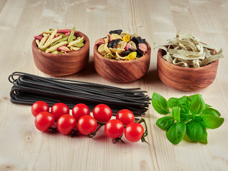 Dried pasta: colorful orechiette, fusilli , tagliatelle, spaghetti, fresh tomatoes and basil, on a wooden board