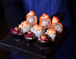 Sushi chef is holding a set of rolls on a black board