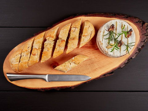 Baked Camembert with walnuts, rosemary stalks and garlic cloves, served with crusty garlic gread, on a rustic board, flat lay
