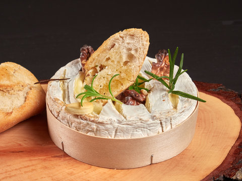 Baked Camembert with walnuts, rosemary stalks and garlic cloves, served with crusty garlic gread, on a rustic board, close-up view