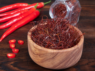 An olive wood bowl filled with thin threads of sun-dried red chili also known as angel hair chili,...