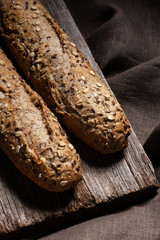 Fresh french bread baguette with seeds on an old wooden board and towel. Healthy food