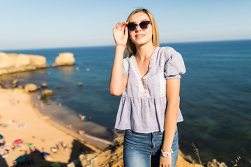 Young pretty woman standing on the edge of the rock coast with beautiful view on the sea coast