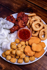 a plate of chicken nuggets, onion rings in tempura, chicken popcorn, rice chips, pieces of fried chicken and mid pepper sauce
