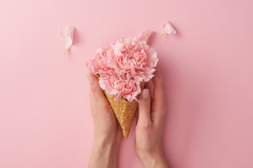 cropped shot of woman holding wafer cone with beautiful tender flowers isolated on pink