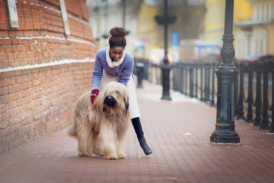 African girl in a coat stroking a dog of Briard breed on a city street on a winter day.