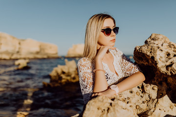 Portrait of active girl on the ocean with flying hair at camera and charming smile on beach with white sand and rocks background