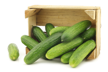 fresh green baby cucumbers in a wooden crate on a white background