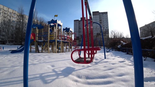 Empty children swings on a playground in city park at sunny winter day, view from the bottom,.