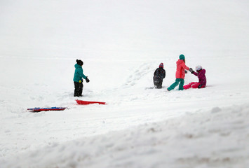 Winter snowy day fun background. View with group of kids enjoying blizzard weather on a slagging spot. Having fun at winter concept.