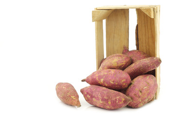 freshly harvested sweet potatoes in a wooden crate on a white background