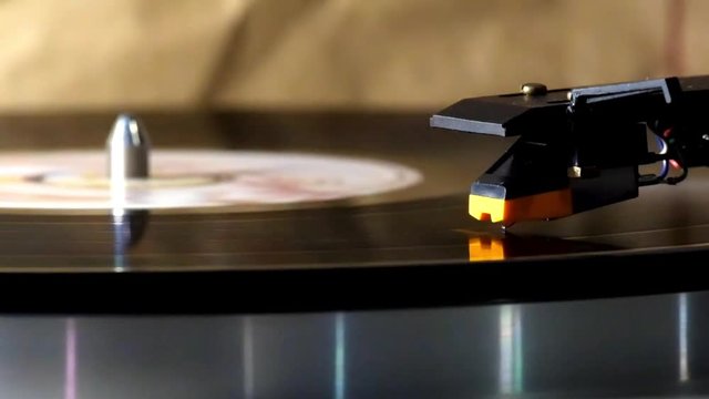 Head-shell cartridge is on a rotating vinyl record. Spinning vinyl record on the analog stereo turntable