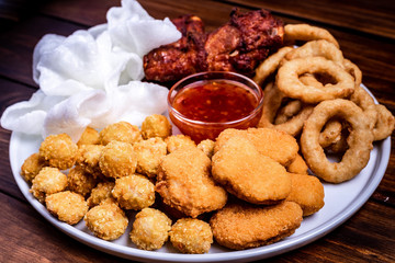 Snacks for beer on a white plate are: chicken nuggets, onion rings in tempura, chicken popcorn and chili sauce.Assortment of fried snacks Onion rings, chicken wings, bread with sauce