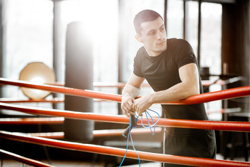 Portrait of a young athletic man in black sportswear standing on the boxxing ring at the gym