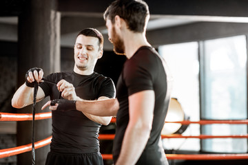 Boxing trainer winding bandage on the wrist for a man, preparing for the boxing on the boxing ring...