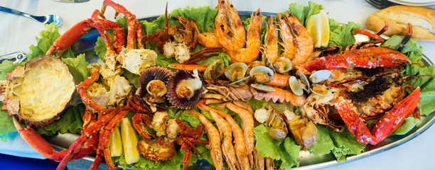 Assortment of grilled seafood with prawns, lobster, clams, crayfish, scallops, spider crab, small crabs and lemon