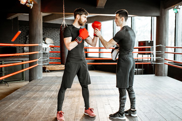 Boxing trainer showing to a man how to fight, teaching to box on the boxing ring at the gym