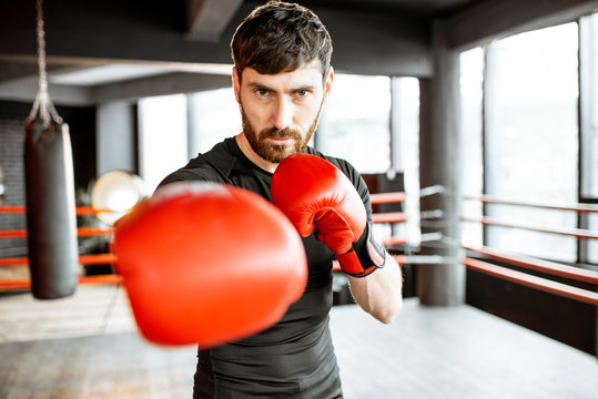 Portrait Of An Athletic Man As A Boxer In Red Boxing Gloves On The Fighting Ring At The Gym