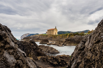 Fototapeta na wymiar Small church of Santa Catalina on the coast of Mundaca village in Biscay during a cloudy day