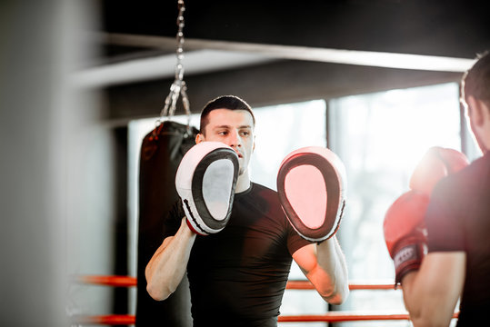 Athletic man fighting during the training with boxing trainer on the boxing ring at the gym